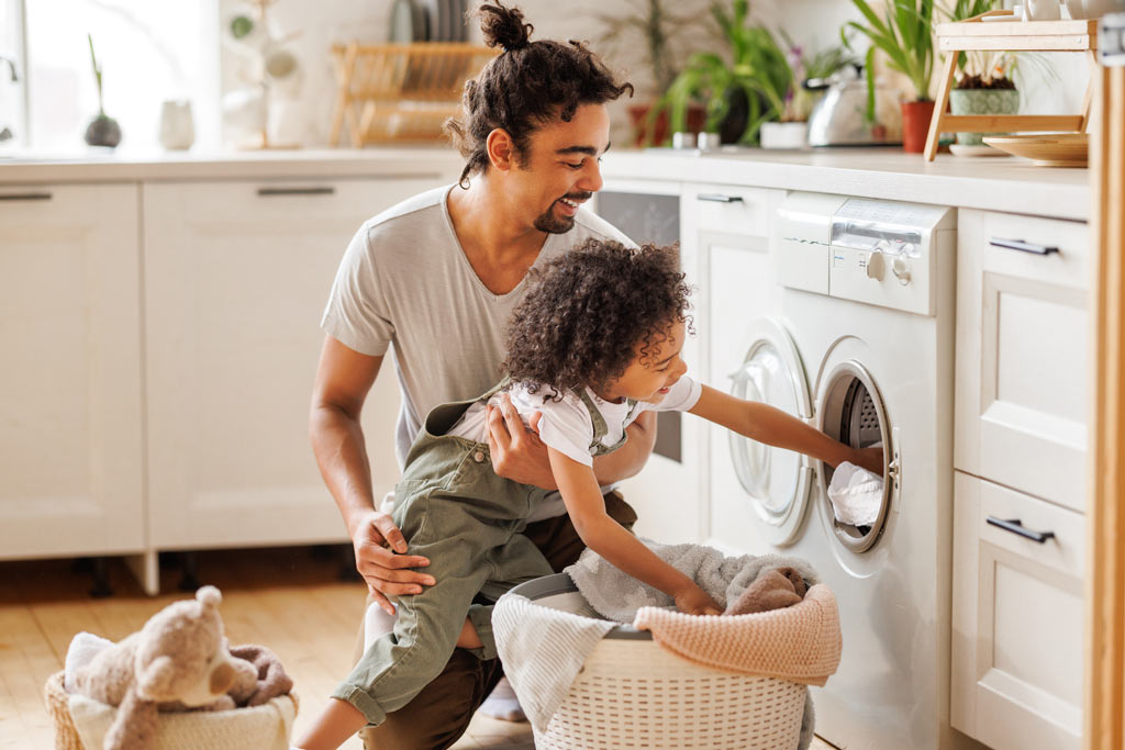 image d'un papa et son enfant partageant un moment de vie devant une machine à laver dans la cuisine
