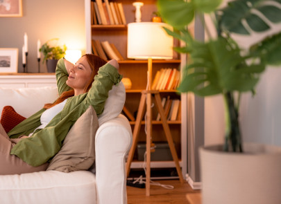 Femme rousse allongée sur un canapé blanc confortable, les mains derrière la tête, les yeux fermés, profitant d'un moment serein de détente dans un salon confortable et lumineux