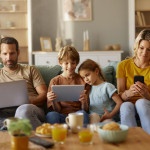 image d'une famille assise dans le salon sur un canapé en train de regarder leurs tablettes connecté en wifi