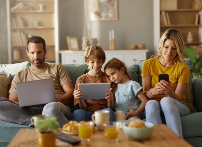 image d'une famille assise dans le salon sur un canapé en train de regarder leurs tablettes connecté en wifi