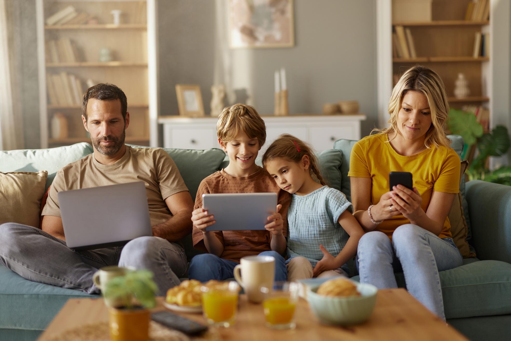 image d'une famille assise dans le salon sur un canapé en train de regarder leurs tablettes connecté en wifi