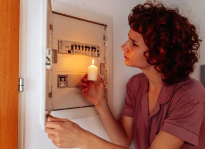 Une image qui représente une femme éclairant un tableau électrique avec une bougie