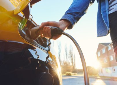 Voiture électrique branchée devant une maison dans une rue au coucher du soleil Rechercher sur Google