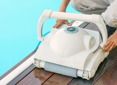 Image d'un aspirateur robot de piscine au bord d'une piscine avec quelqu'un qui tient le robot à 2 mains