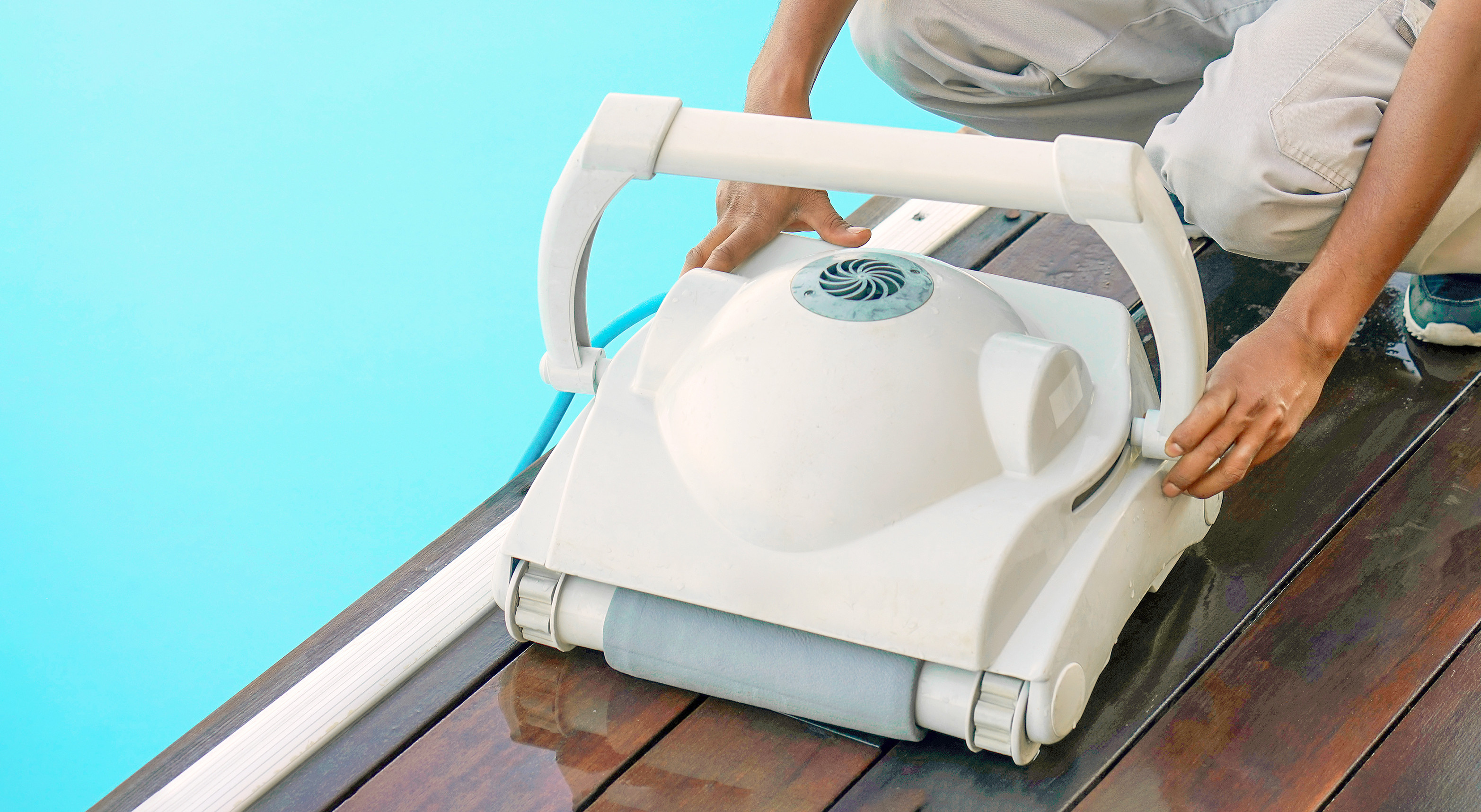 Image d'un aspirateur robot de piscine au bord d'une piscine avec quelqu'un qui tient le robot à 2 mains