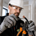 Artisan électricien manipulant un conducteur souple multibrins sur un chantier de rénovation résidentielle.